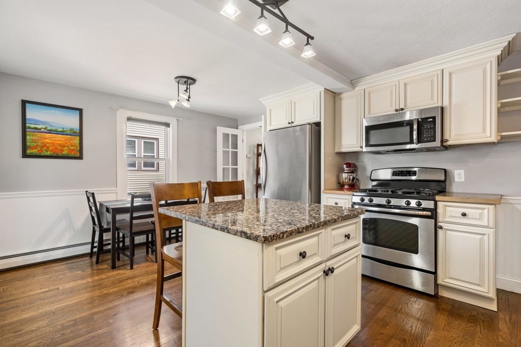 33 Bromfield Street, Unit 33 Watertown, MA 02472 - Photo 7 of 21 a kitchen with stainless steel appliances granite countertop a stove a refrigerator a microwave a dining table and chairs with wooden floor