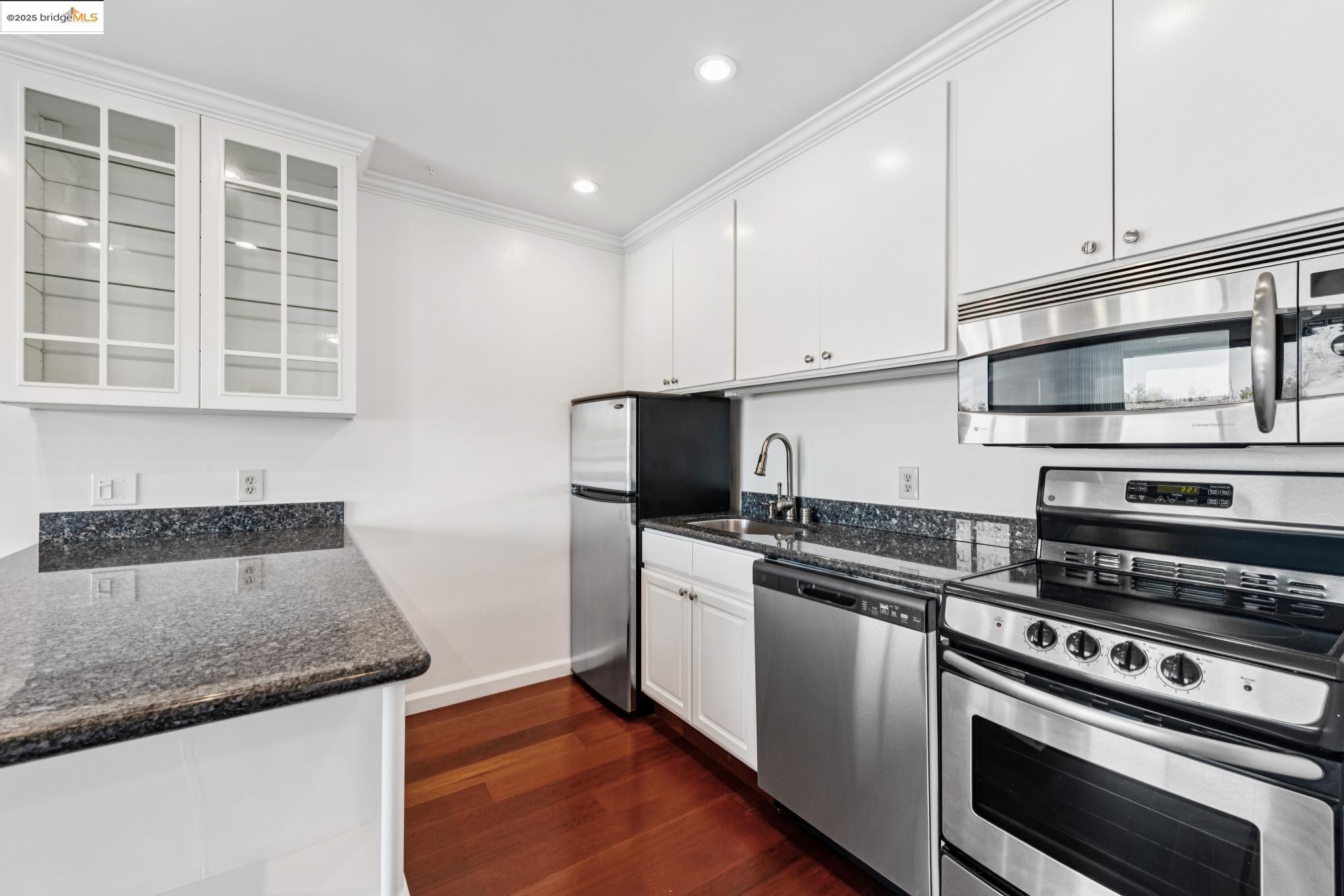 1 Embarcadero, Unit 161 Oakland, CA 94607 - Photo 26 of 31 Kitchen featuring stainless steel appliances, white cabinetry, glass insert cabinets, dark wood-type flooring, and dark stone counters