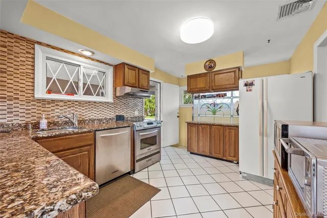 a kitchen with stainless steel appliances granite countertop a refrigerator a stove and a sink with wooden cabinets