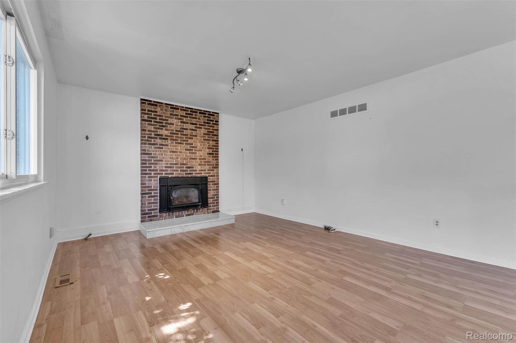 7000 Woonsocket Street Canton, MI 48187 - Photo 26 of 65 Spacious room with a brick-surround fireplace and black insert, complemented by a light-toned wood-finish floor