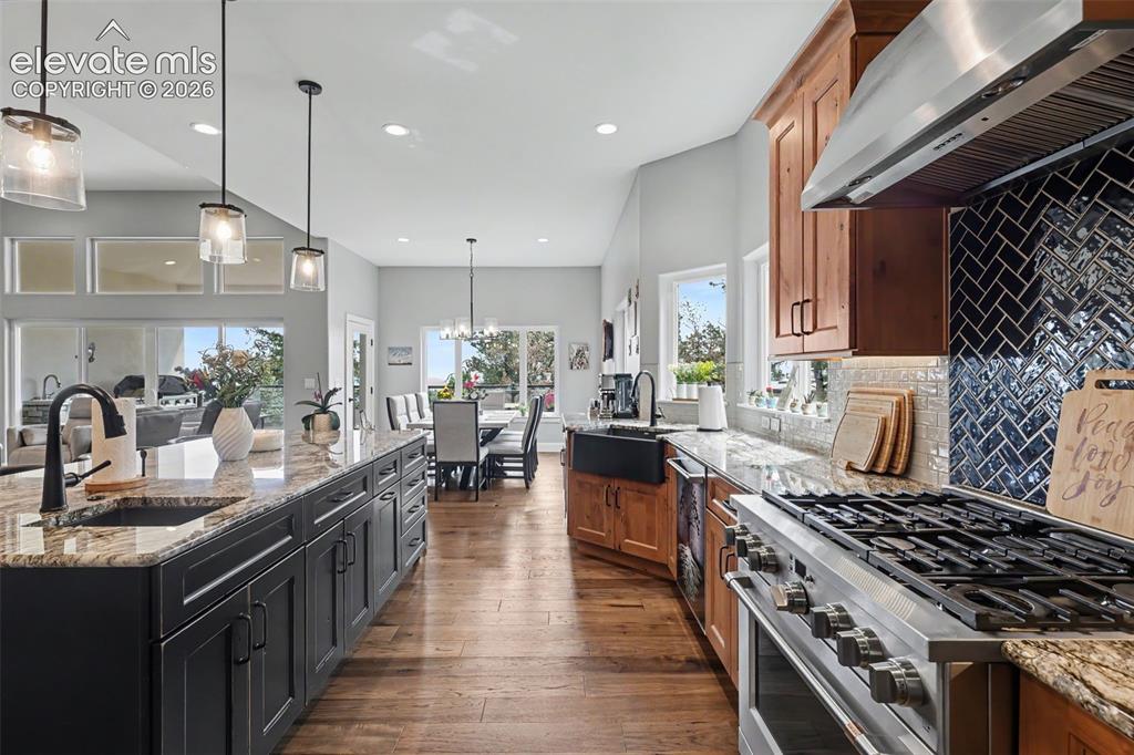 21 Leaming Road Colorado Springs, CO 80906 - Photo 22 of 48 Spacious kitchen featuring an expansive island with granite countertops and a black undermount sink, rich wood-finish flooring, and a professional-grade stainless steel range with a herringbone tile backsplash