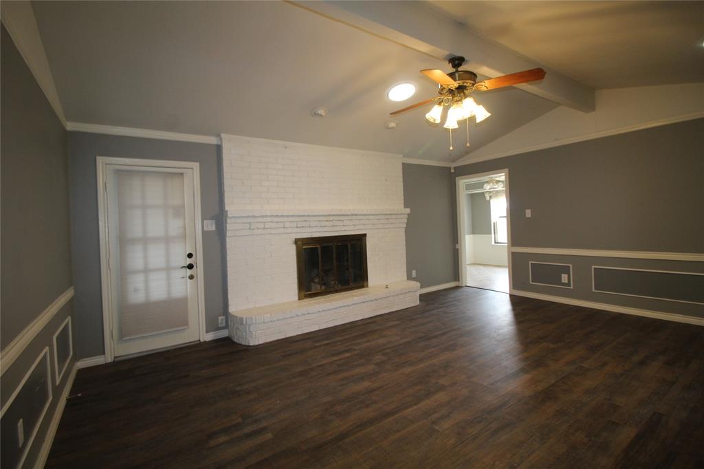 634 Ray Avenue DeSoto, TX 75115 - Photo 4 of 28 Unfurnished living room featuring wood finished floors, vaulted ceiling with beams, ceiling fan, a brick fireplace, and visible vents