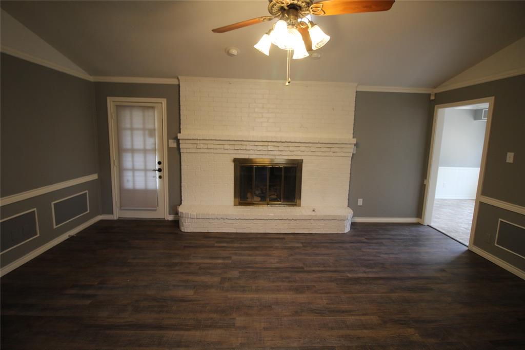 634 Ray Avenue DeSoto, TX 75115 - Photo 5 of 28 Unfurnished living room featuring vaulted ceiling, wood finished floors, a brick fireplace, ceiling fan, and ornamental molding