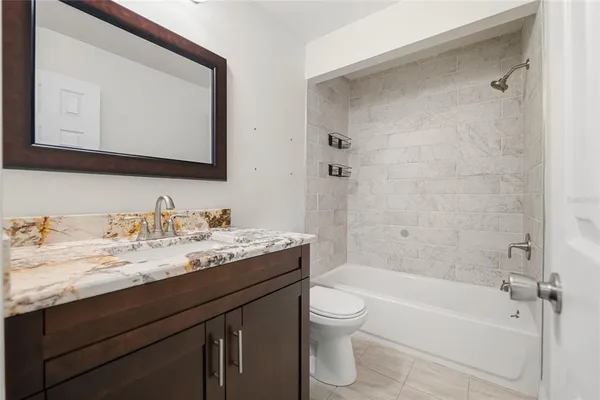 a bathroom with a granite countertop bathtub sink vanity mirror and toilet