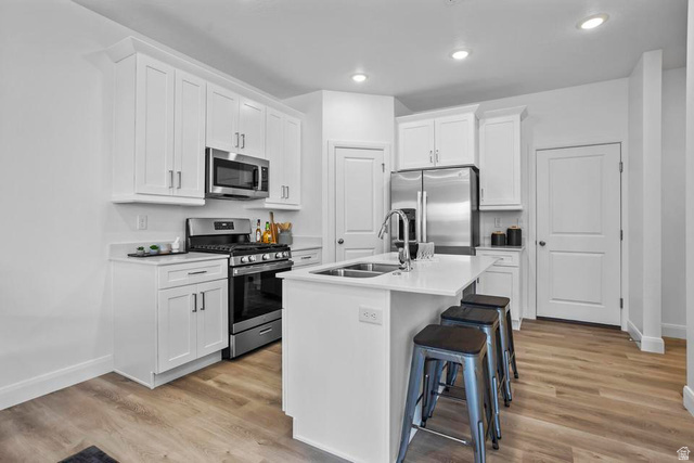 488 West Greenstone Pl Street, Unit 1010 St. George, UT 84790 - Photo 14 of 34 Modern kitchen featuring white cabinetry, stainless steel appliances, a center island with a double sink, light-toned countertops, and wood-finish flooring