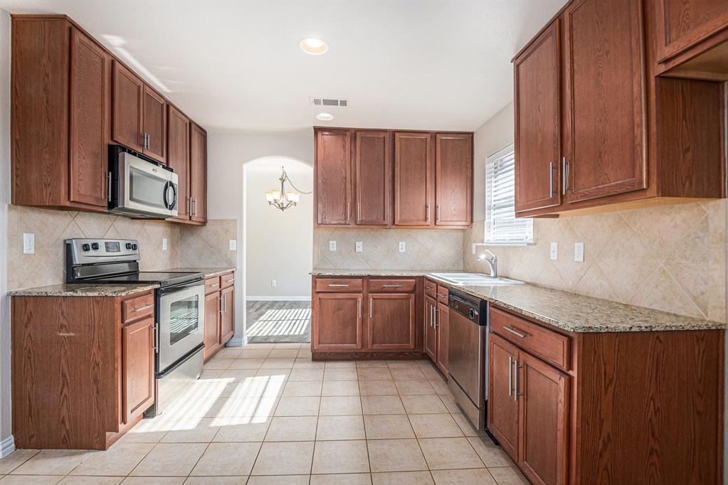 8313 Water Buck Run Fort Worth, TX 76179 - Photo 12 of 25 a kitchen with stainless steel appliances granite countertop wooden cabinets a stove top oven a sink and dishwasher