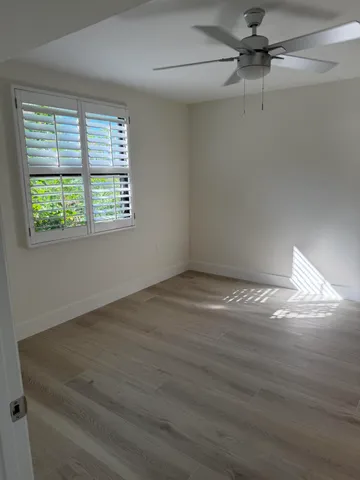 an empty room with wooden floor fan and windows