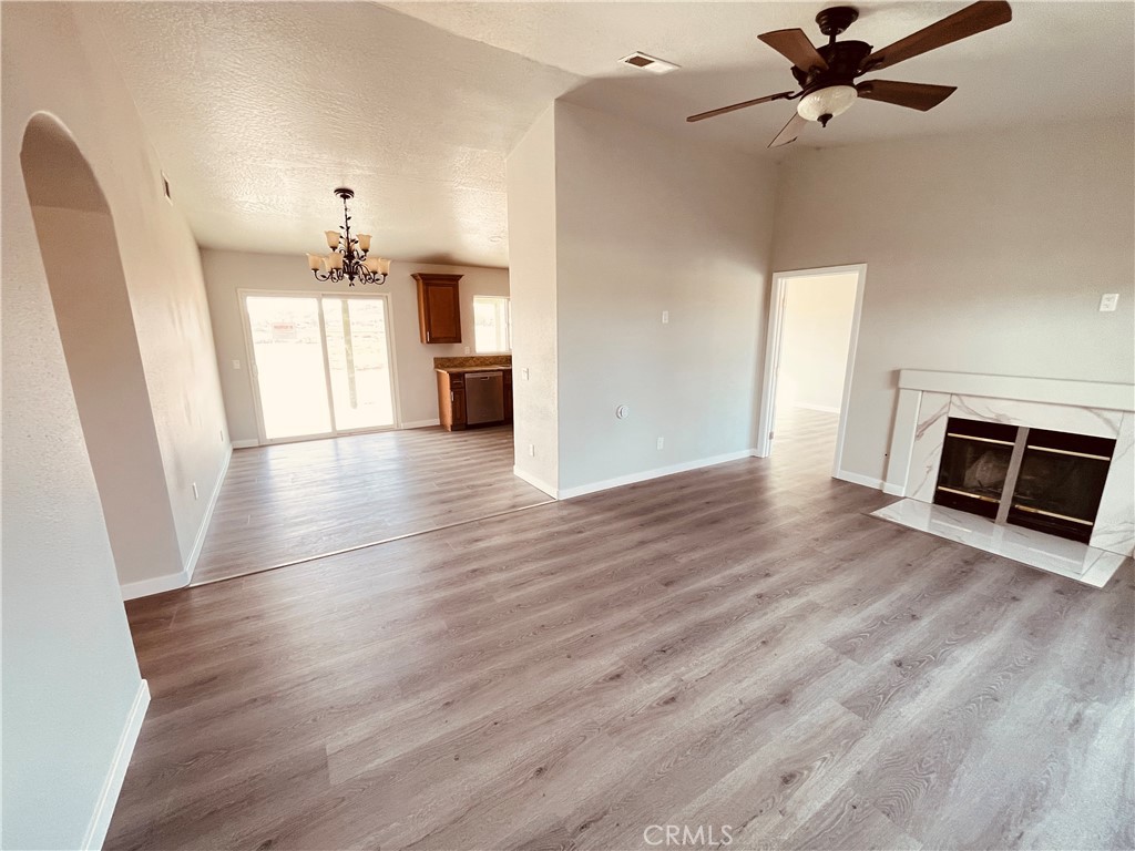 20891 Thunderbird Road Apple Valley, CA 92307 - Photo 11 of 45 an empty room with wooden floor a ceiling fan a fireplace and windows