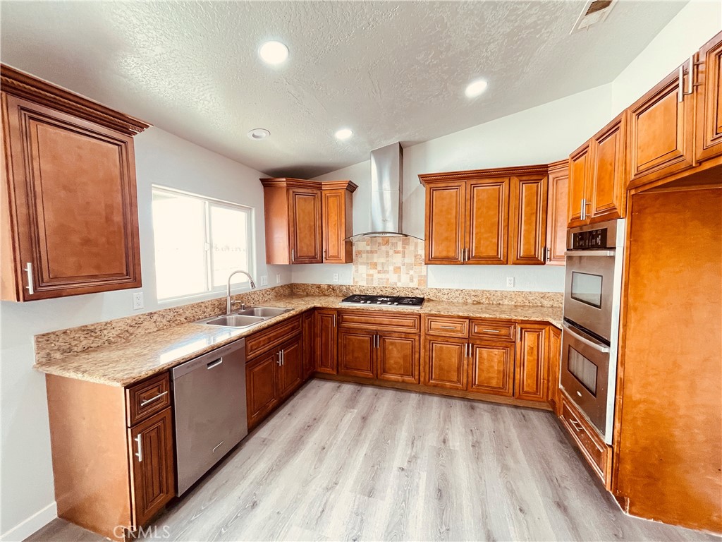 20891 Thunderbird Road Apple Valley, CA 92307 - Photo 20 of 45 a kitchen with stainless steel appliances granite countertop wooden cabinets a sink and dishwasher a refrigerator with wooden floor