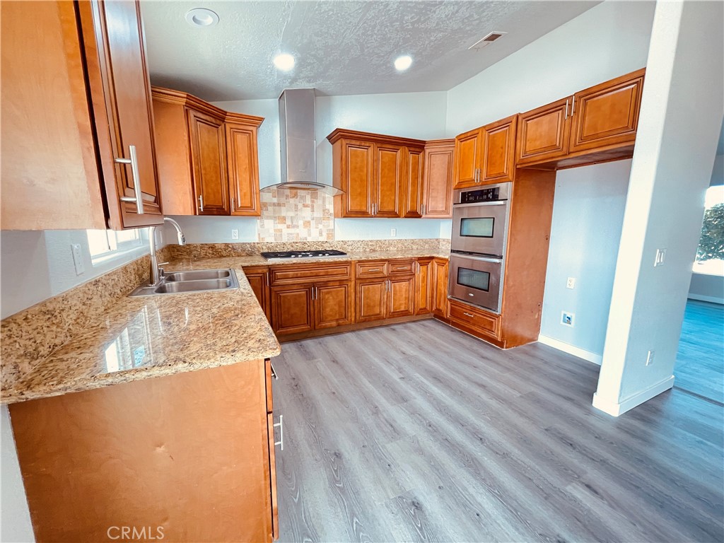 20891 Thunderbird Road Apple Valley, CA 92307 - Photo 21 of 45 a kitchen with stainless steel appliances granite countertop wooden cabinets a refrigerator a sink a stove a microwave and wooden floors