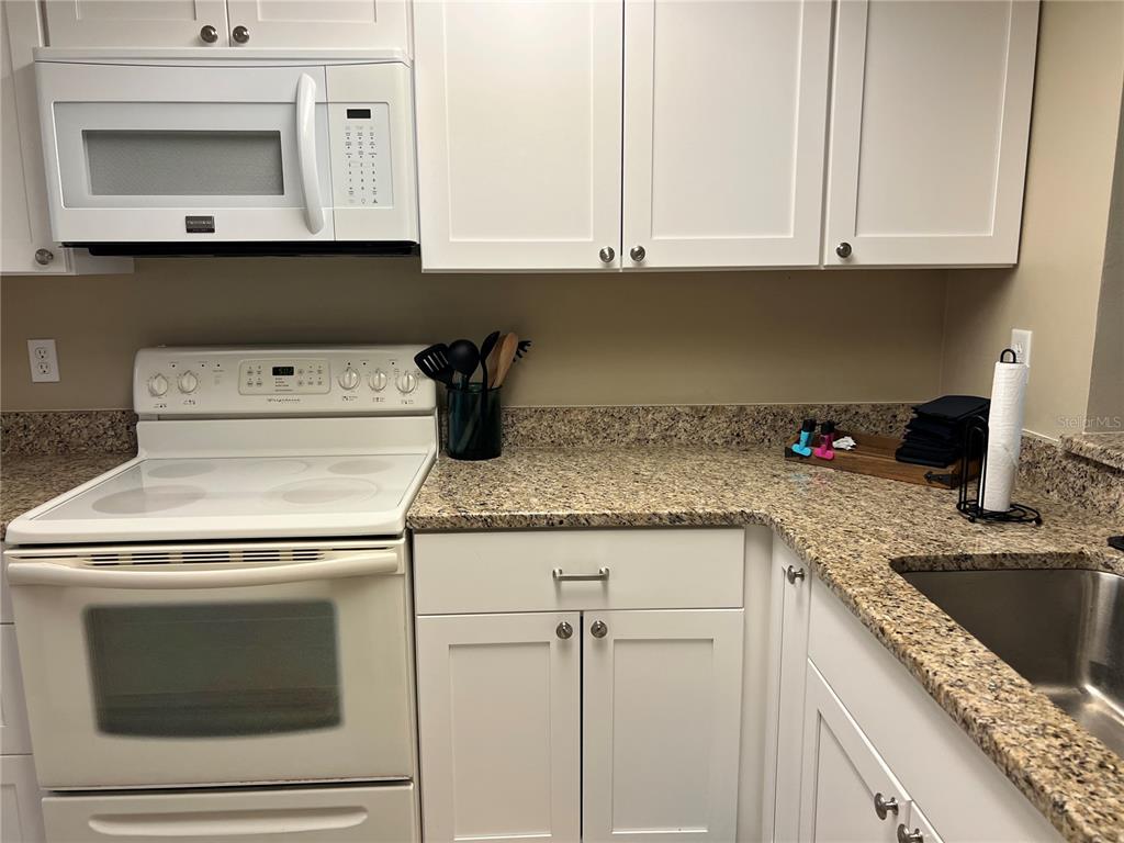 9609 Midiron Court, Unit 1 New Port Richey, FL 34655 - Photo 7 of 16 a kitchen with granite countertop white cabinets and white appliances