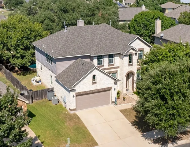 an aerial view of a house with yard and trees in the background