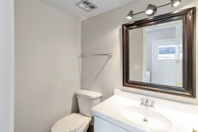88 West 50 South, Unit J10 Centerville, UT 84014 - Photo 10 of 19 Bathroom featuring a white vanity with an integrated sink, a dark wood-framed mirror with track lighting, and a white toilet