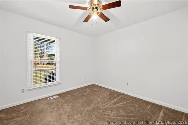 an empty room with chandelier fan and windows