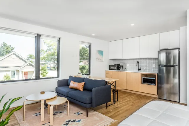a living room with stainless steel appliances furniture a rug and a kitchen