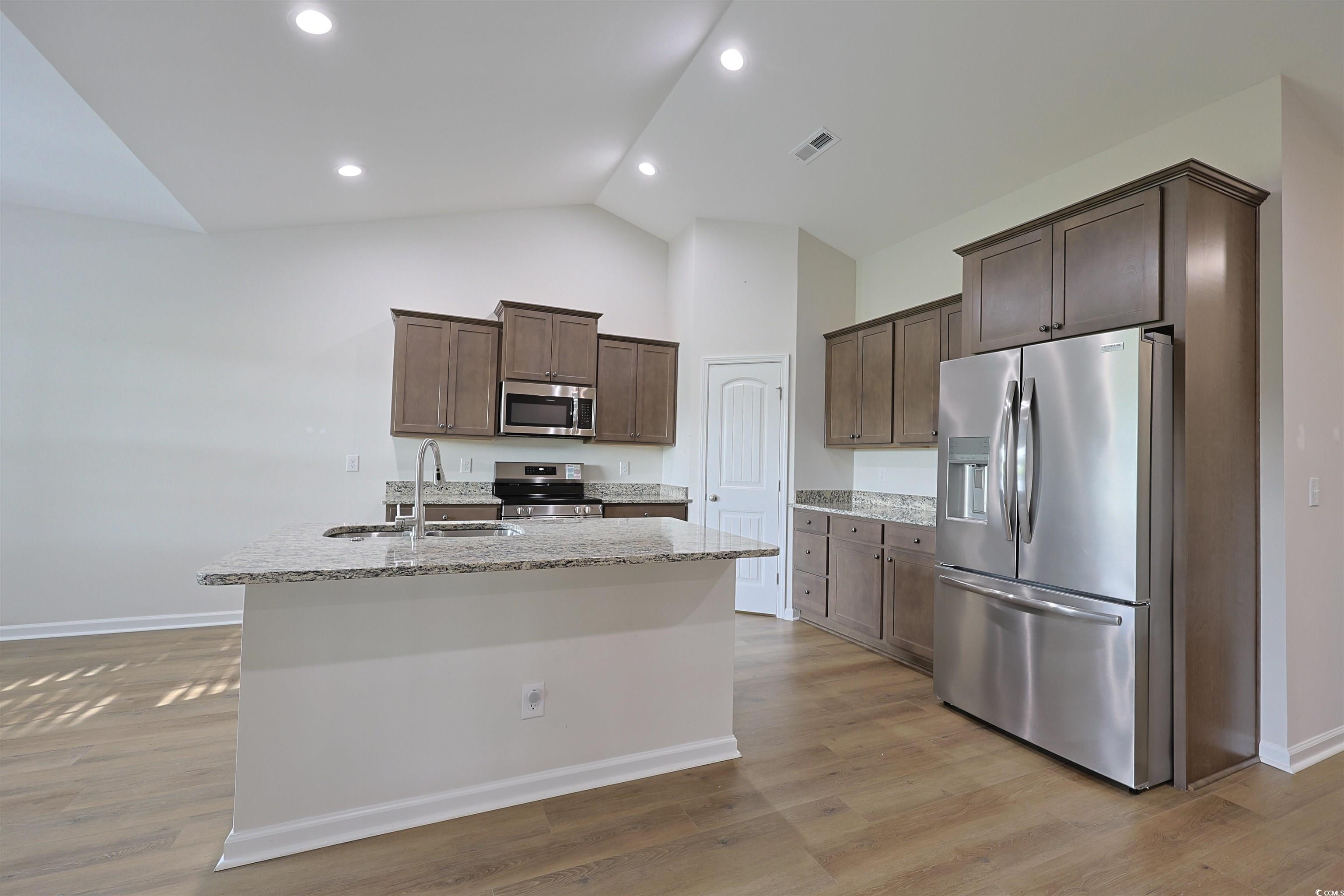 266 Ole Maple Street Loris, SC 29569 - Photo 5 of 30 Kitchen with stainless steel appliances, dark brown cabinetry, an island with sink, light stone counters, and light wood-type flooring