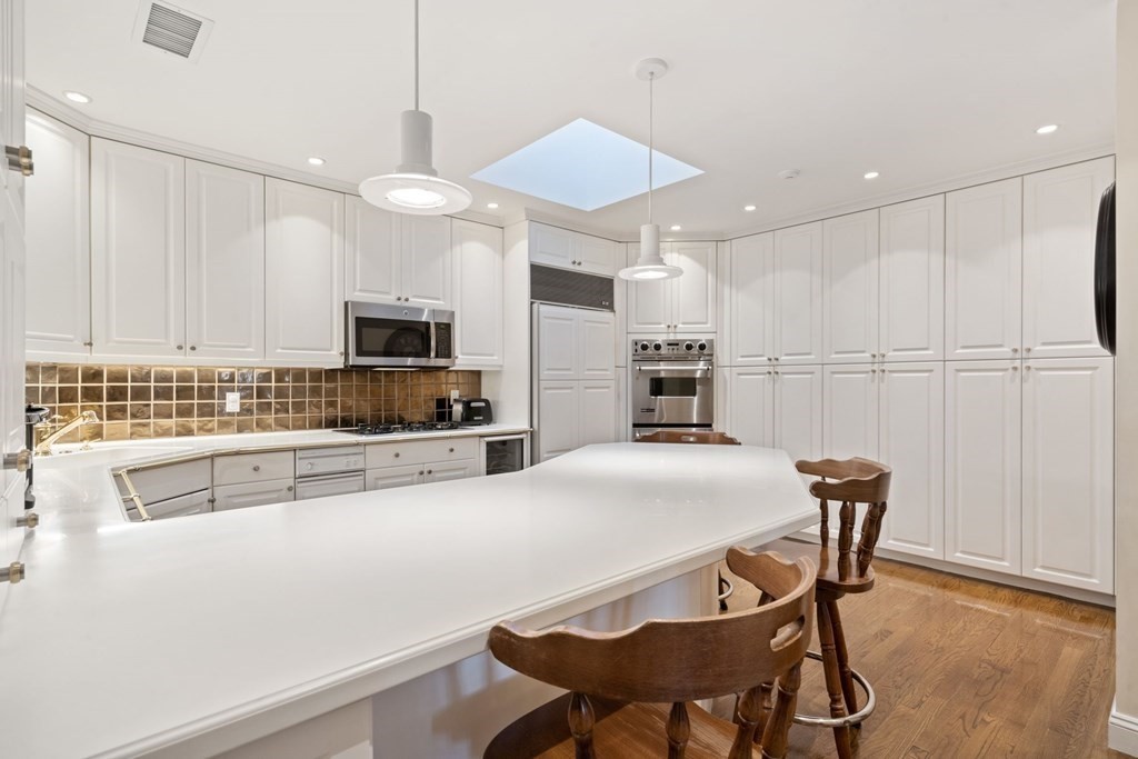 49 Rawson Road, Unit 49 Brookline, MA 02445 - Photo 9 of 42 a kitchen with stainless steel appliances kitchen island granite countertop a table chairs and a refrigerator