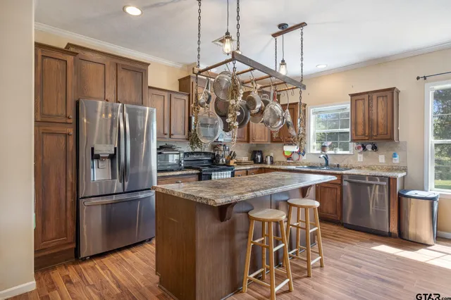 a kitchen with stainless steel appliances granite countertop a refrigerator a sink dishwasher a kitchen island with wooden cabinets and floor