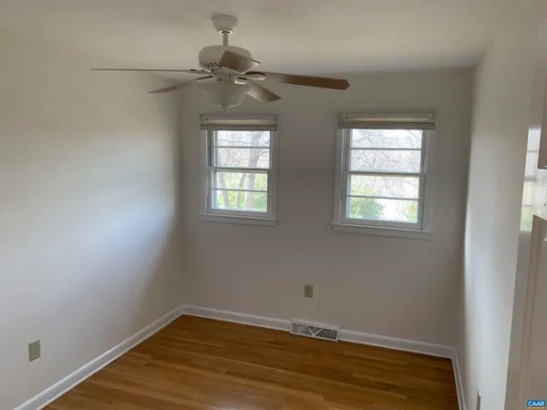an empty room with wooden floor fan and windows
