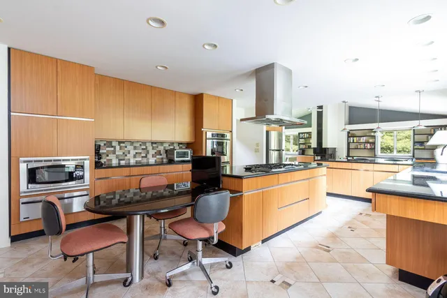 a kitchen with stainless steel appliances kitchen island granite countertop a table chairs sink and cabinets