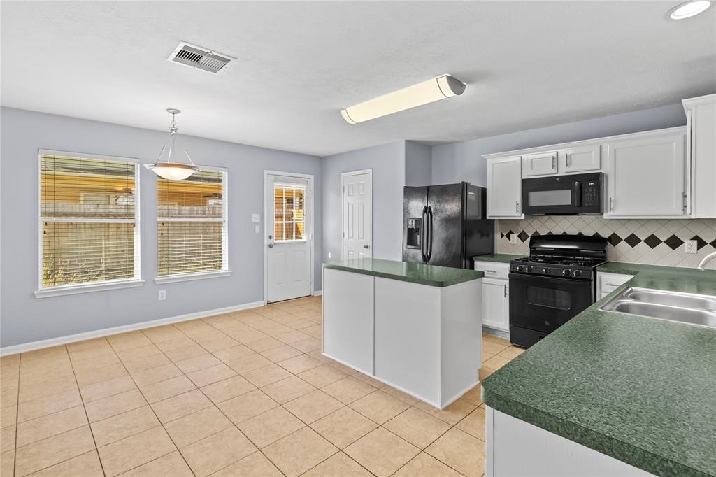 7454 Riven Oaks Court Cypress, TX 77433 - Photo 14 of 18 Bright kitchen with natural light, featuring white cabinets, green countertops, and black appliances. There's a central island, tiled floors, and a cozy dining area with large windows.