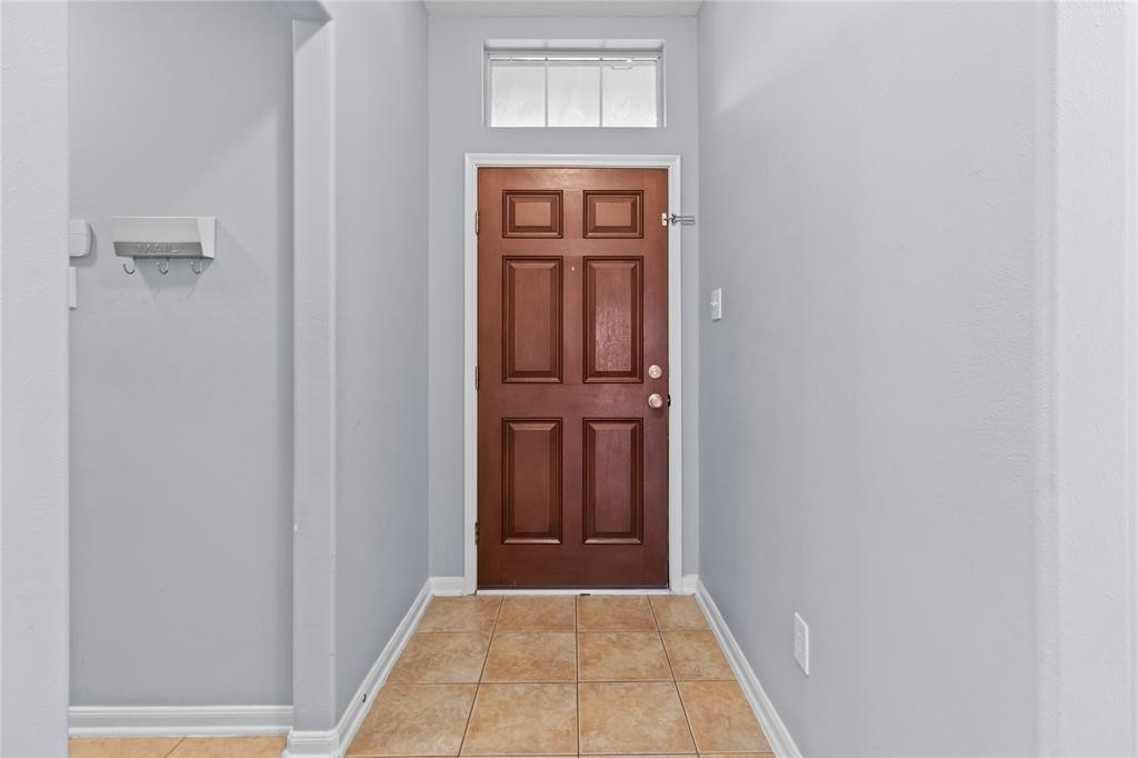 7454 Riven Oaks Court Cypress, TX 77433 - Photo 2 of 18 This welcoming entryway features a rich wooden door with a transom window above, neutral gray walls, and tiled flooring.