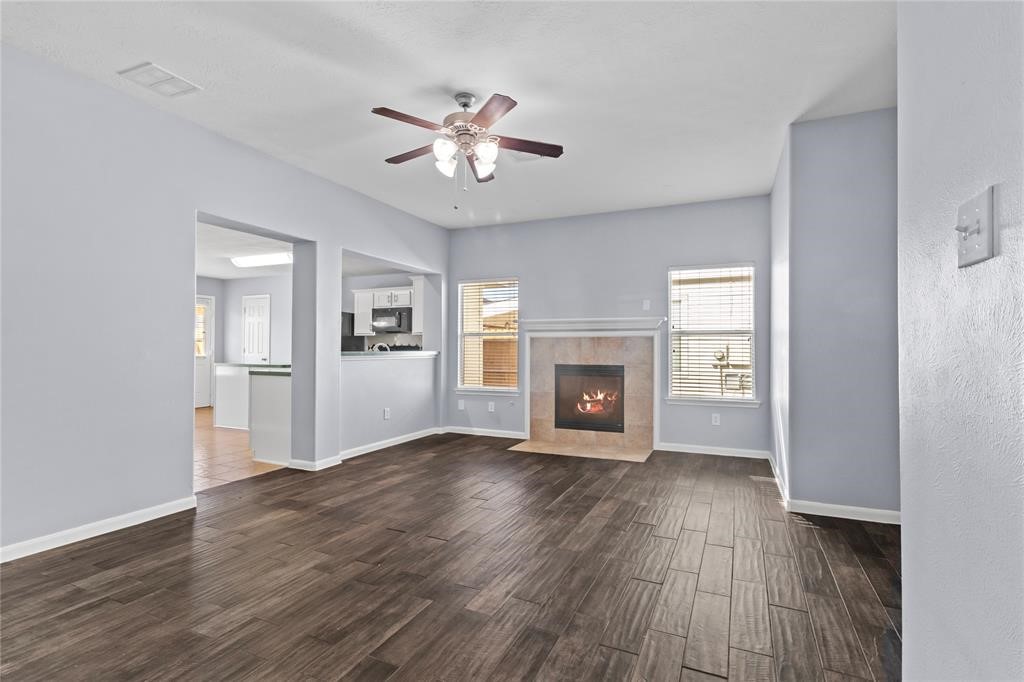 7454 Riven Oaks Court Cypress, TX 77433 - Photo 3 of 18 This spacious living area features elegant dark wood flooring, a cozy fireplace, and ample natural light from two large windows. The open layout connects seamlessly to the kitchen, creating a welcoming atmosphere perfect for entertaining.