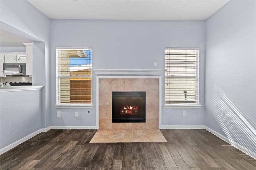 7454 Riven Oaks Court Cypress, TX 77433 - Photo 5 of 18 Cozy living area featuring a modern gas fireplace with a tile surround, flanked by two large windows for natural light. The space has stylish wood-look flooring and an open view into the adjacent kitchen.