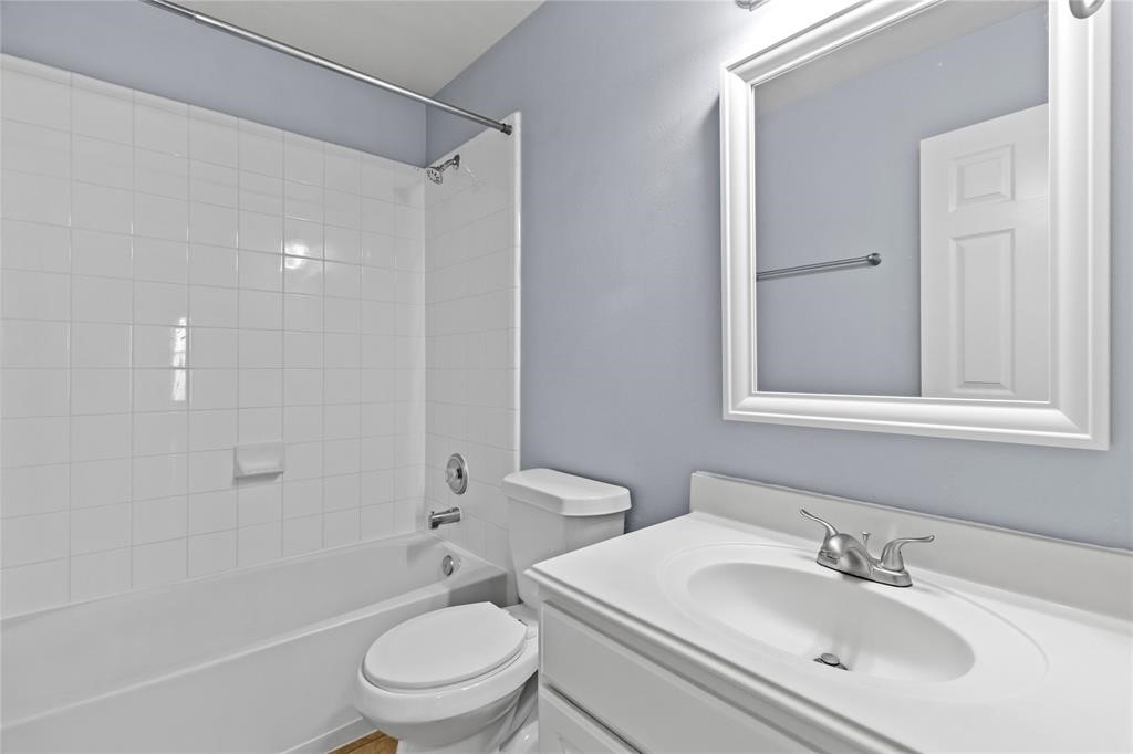 7454 Riven Oaks Court Cypress, TX 77433 - Photo 8 of 18 This bathroom features a clean, modern design with light-colored walls and tile. It includes a bathtub with a shower, a vanity with a sink, and a large mirror, creating a bright and functional space.