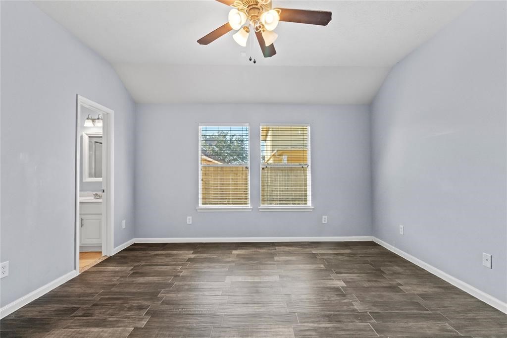 7454 Riven Oaks Court Cypress, TX 77433 - Photo 9 of 18 This room features light gray walls and dark wood-look tile flooring, with a ceiling fan and two windows providing natural light. There's an entrance to an en-suite bathroom, making it ideal for a bedroom.