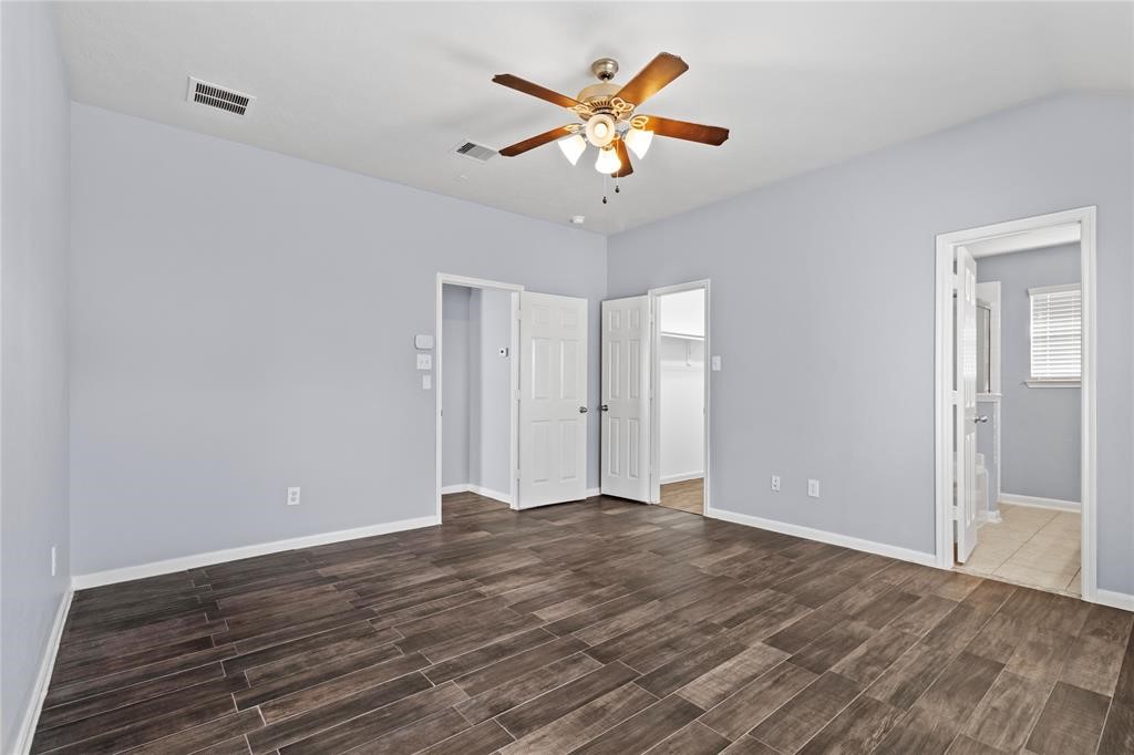 7454 Riven Oaks Court Cypress, TX 77433 - Photo 10 of 18 This spacious bedroom features light gray walls, wood-look tile flooring, and a ceiling fan. It includes access to a walk-in closet and an en-suite bathroom, creating a comfortable and practical living space.