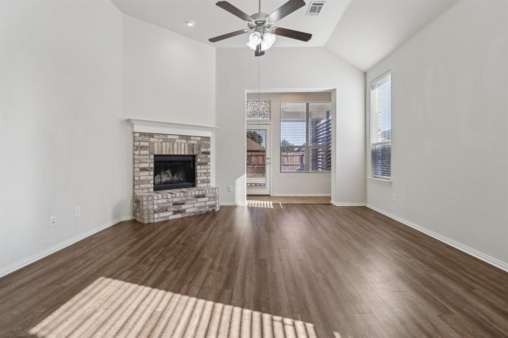 588 Louder Way Fate, TX 75087 - Photo 5 of 34 Unfurnished living room with dark wood-type flooring, a fireplace with raised hearth, lofted ceiling, and ceiling fan