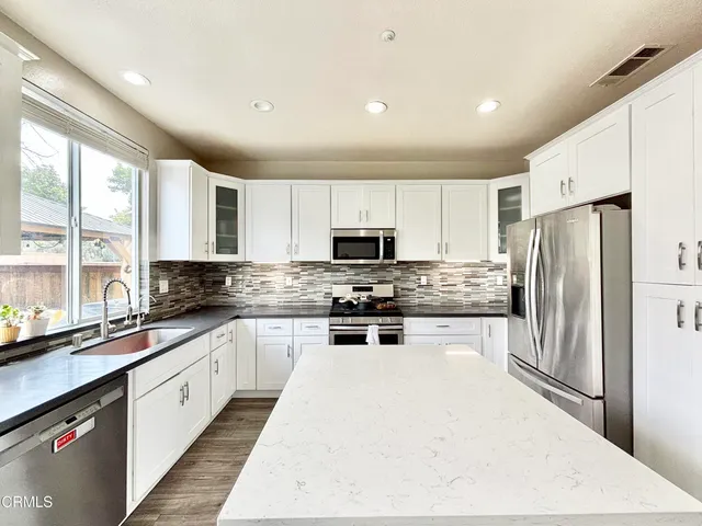 a large kitchen with stainless steel appliances granite countertop a stove a sink a refrigerator and white cabinets