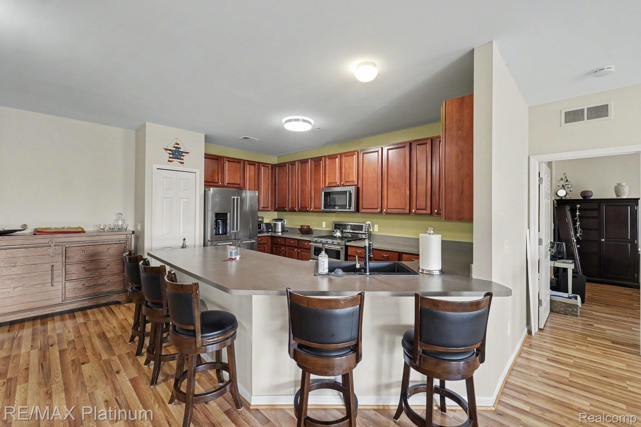 10217 Crossview Trail Howell, MI 48855 - Photo 11 of 26 Kitchen featuring a substantial breakfast bar, stainless steel appliances, rich wood-finish cabinetry, a double basin sink, and wood-finish flooring