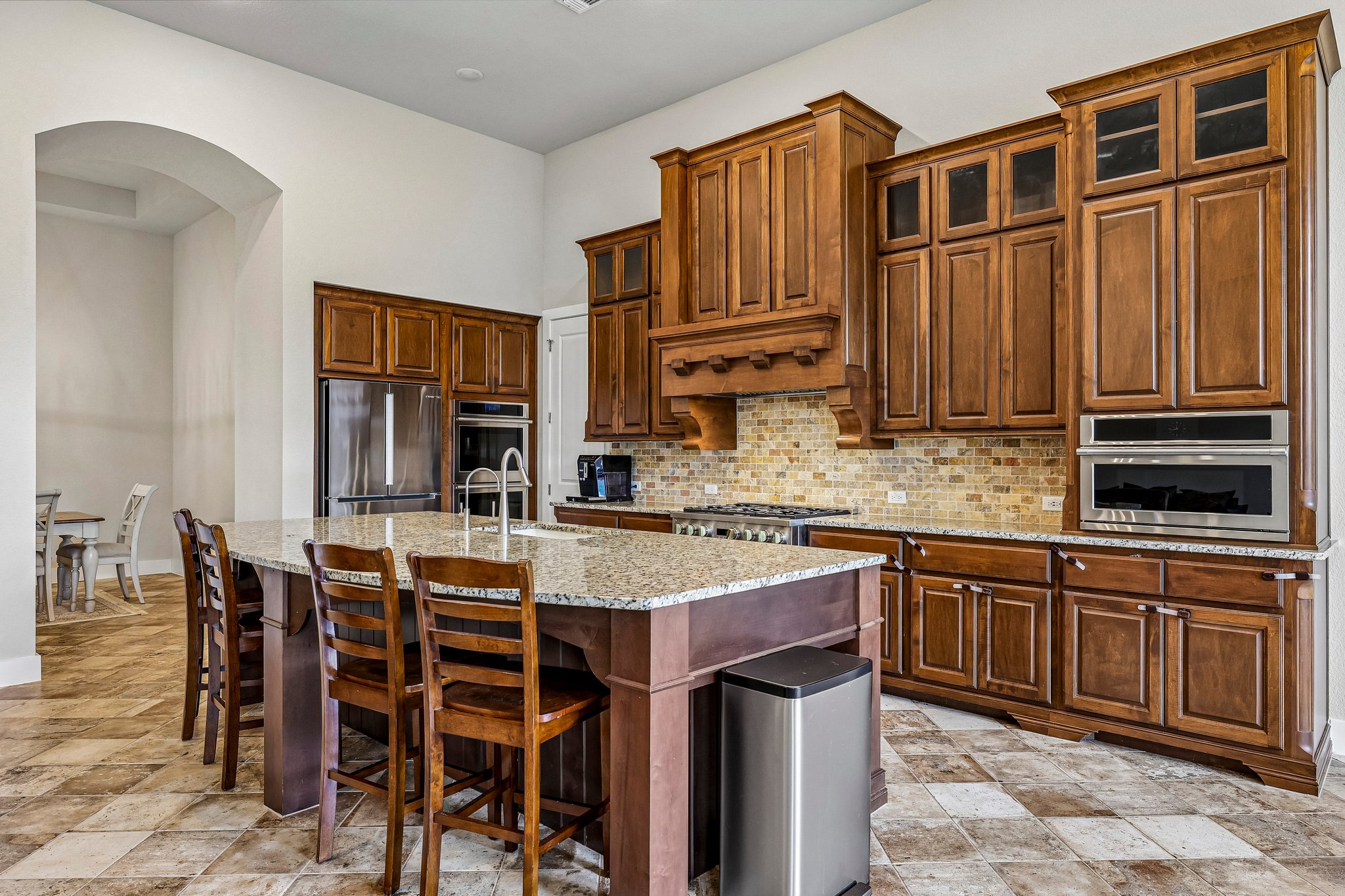 A grand chef's kitchen features rich wood cabinetry, natural stone counters, and an inviting breakfast bar.