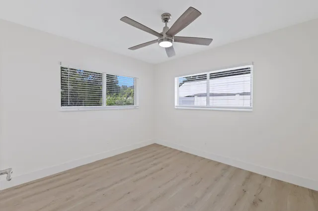 a view of an empty room with wooden floor and ceiling fan