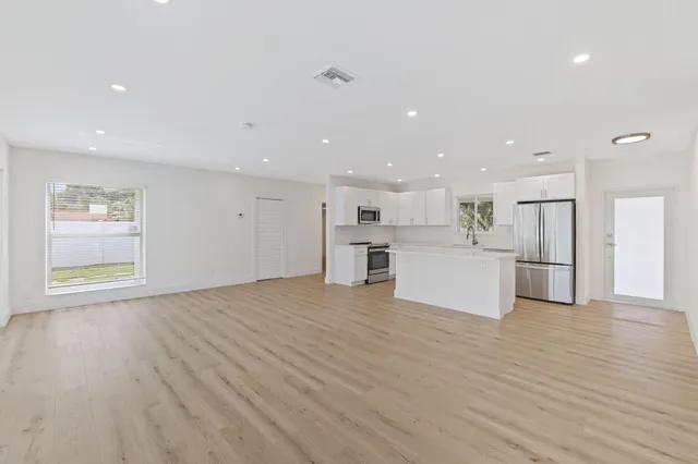 a large white kitchen with kitchen island a sink wooden floor and a refrigerator