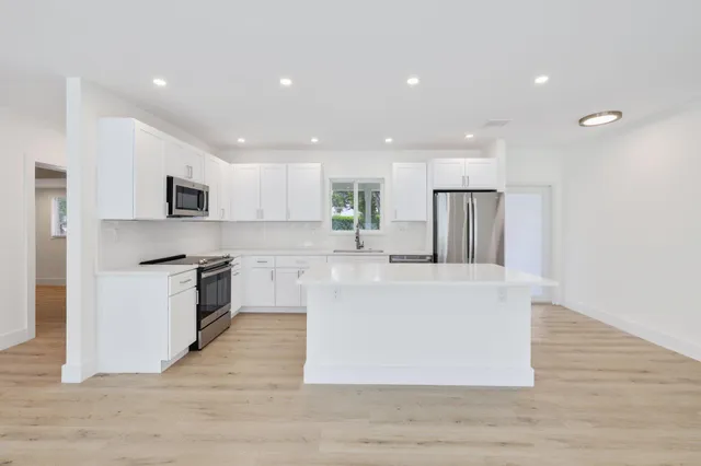 a large kitchen with stainless steel appliances granite countertop a large center island a stove a refrigerator white cabinets and wooden floor