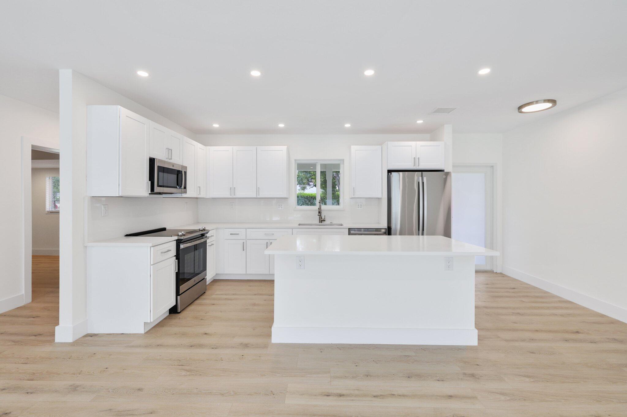 1198 Southwest 3rd Street Boca Raton, FL 33486 - Photo 10 of 29 a large kitchen with stainless steel appliances granite countertop a large center island a stove a refrigerator white cabinets and wooden floor