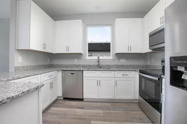 a kitchen with granite countertop white cabinets sink and stainless steel appliances