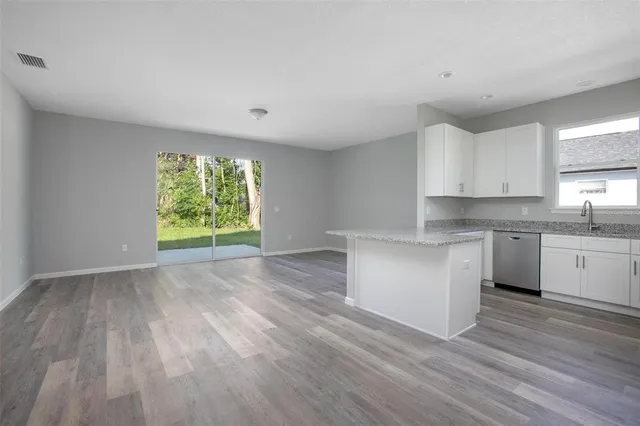 a open kitchen with granite countertop a stove top oven a sink dishwasher and white cabinets with wooden floor