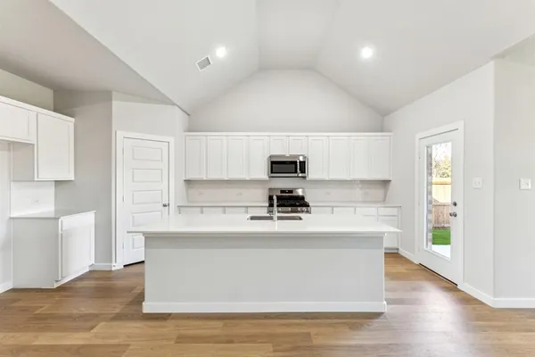 a view of kitchen with stainless steel appliances granite countertop a stove top oven a sink dishwasher and white cabinets with wooden floor