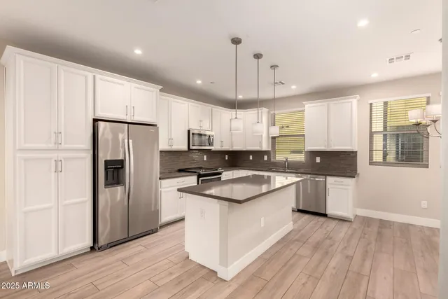 a kitchen with stainless steel appliances granite countertop a refrigerator a sink dishwasher a stove and white countertops with wooden floor