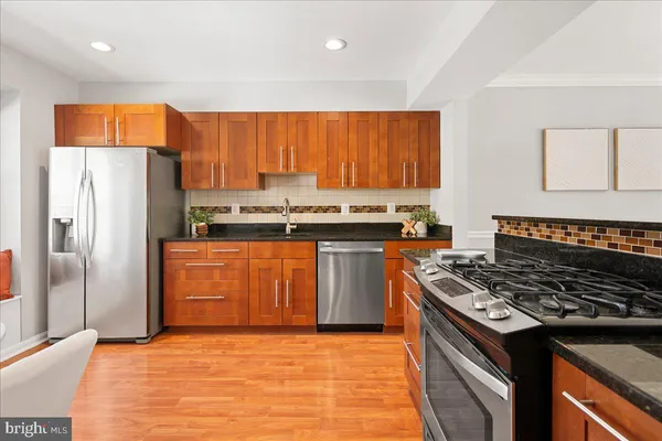 a kitchen with stainless steel appliances granite countertop a stove a refrigerator a sink dishwasher and wooden cabinets with wooden floor