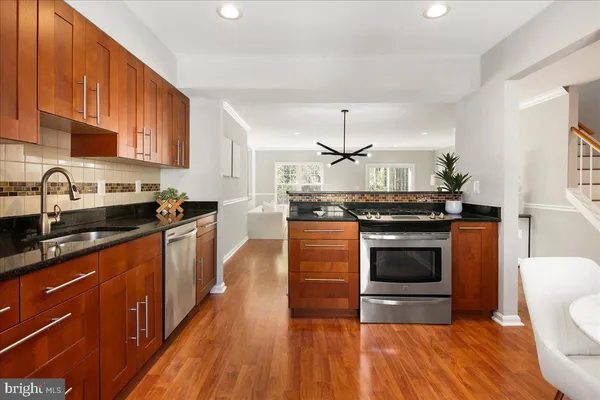 a kitchen with stainless steel appliances granite countertop a refrigerator a sink dishwasher a stove and white countertops with wooden floor