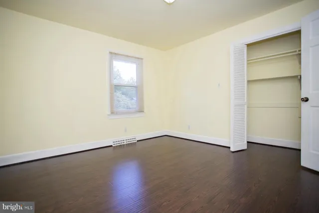 an empty room with wooden floor closet and windows
