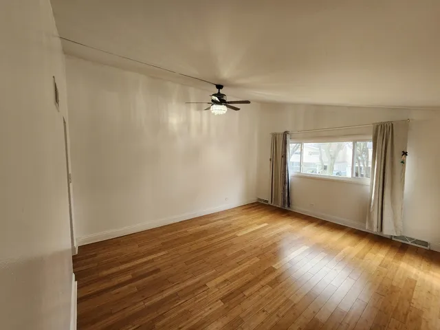 an empty room with wooden floor fan and windows