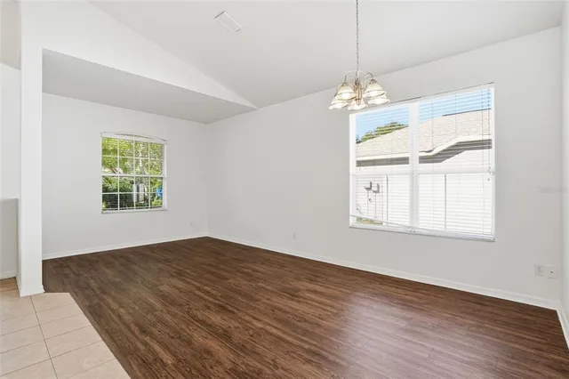 an empty room with wooden floor chandelier and windows