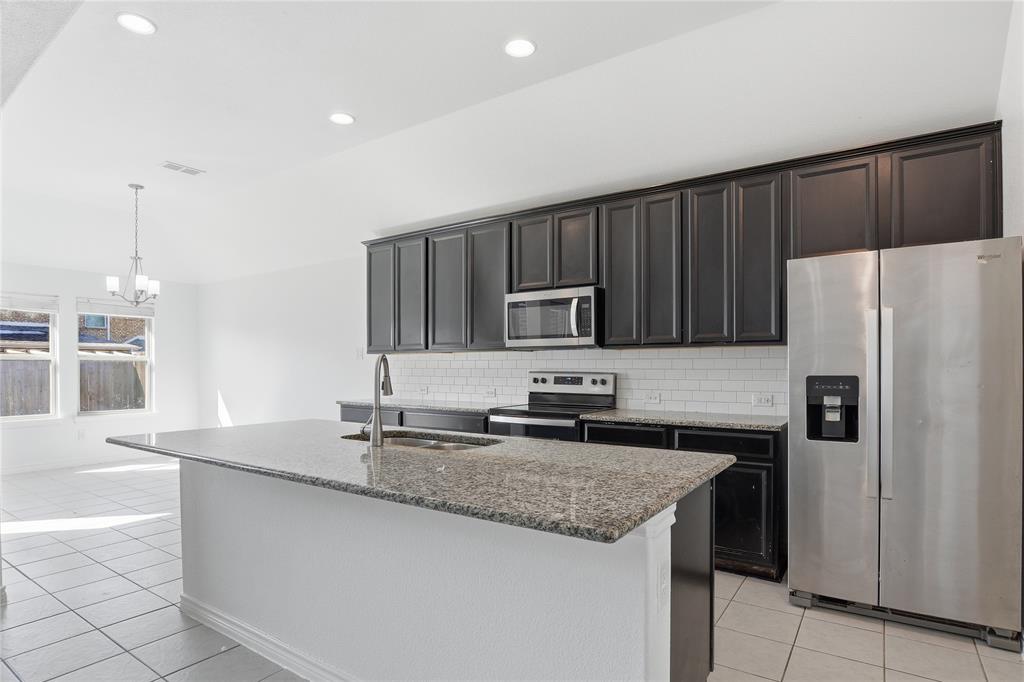 339 Blanco Drive Forney, TX 75126 - Photo 13 of 24 Kitchen with stainless steel appliances, decorative backsplash, dark stone countertops, a center island with sink, and light tile patterned flooring