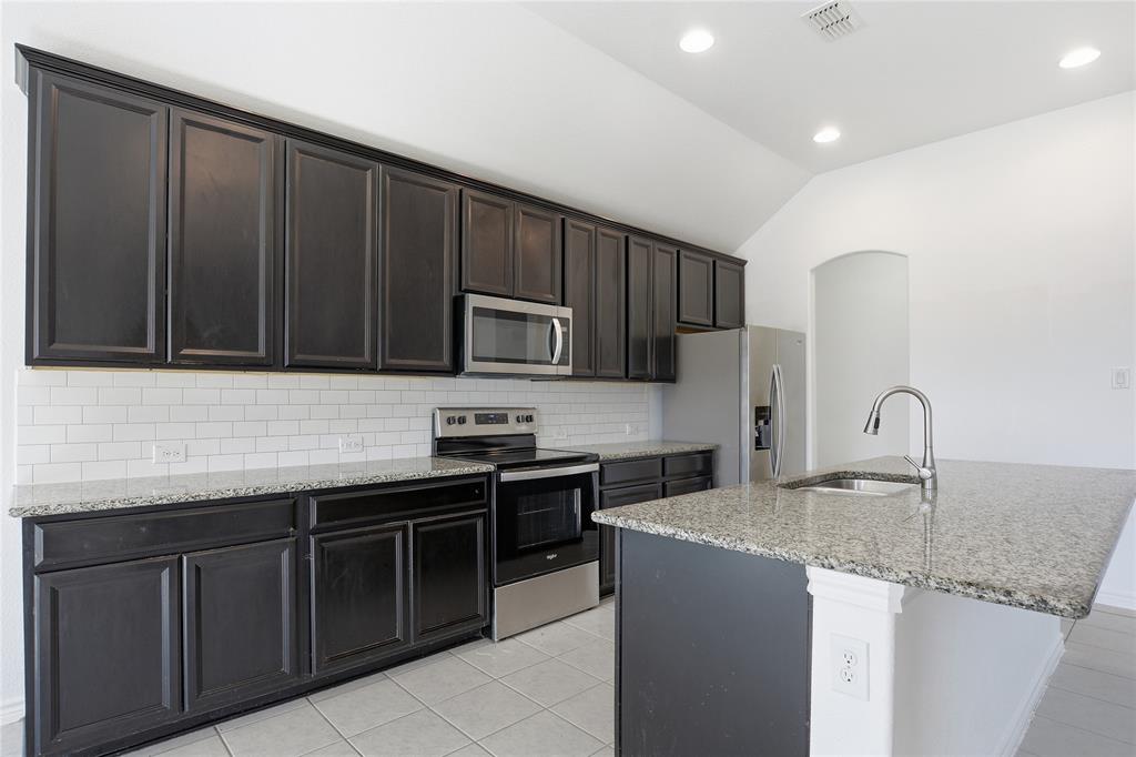 339 Blanco Drive Forney, TX 75126 - Photo 14 of 24 Kitchen featuring stainless steel appliances, light stone counters, a kitchen island with sink, lofted ceiling, and tasteful backsplash